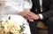 Hands of the bride and groom in a white dress, a bouquet of beige roses