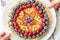 Hands carrying homemade shortcrust pastry cake with mixed berries, raspberries, strawberries and blueberries, isolated on white