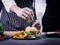 Hands of chef preparing hamburger on wooden cutting board, knife is pinned on the bread, fast food concept