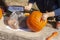 Hands of child cutting out jack-o-lantern from pumpkin with carving knife-holding pumpkin by mouth and working hard at it