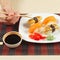 Hands with chopsticks and assorted sushi and soy sauce on black and red bamboo mat.