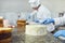 Hands confectioner spreads custard on a white cake on the table in the pastry shop