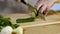 Hands of the cook knife big kitchen a fresh green cucumber on a chopping board from a tree