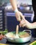 Hands of the cook are pouring the seasoning into the frying pan