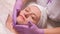 The hands of a cosmetologist in lilac gloves put a soap solution on the female face. Middle-aged woman on the procedure in the