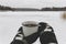 Hands in cozy gloves holding warm cup of tea on background of  snow lake in winter. Hiking and traveling in cold winter season.