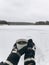 Hands in cozy gloves holding warm cup of tea on background of  snow lake in winter. Hiking and traveling in cold winter season.