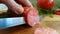 Hands cut sausage salami tomato on a wooden background