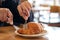 Hands cutting a piece of croissant by knife and fork for breakfast on wooden table