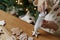 Hands decorating gingerbread cookies with icing and cute dog helping tasting and licking sugar paste on background of christmas