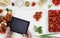 hands with digital tablet above on white cutting board with vegetables and tomatoes food ingredients on kitchen white worktop, co