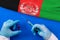 Hands of doctor holding syringe and coronavirus COVID-19 vial vaccine on flag Afghanistan