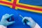 Hands of doctor holding syringe and coronavirus COVID-19 vial vaccine on flag Aland