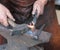 Hands of an elderly blacksmith working iron with a hammer and th