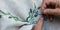 Hands of an elderly woman embroidering a cross-stitch floral pattern on linen fabric. Embroidery. Closeup