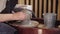 Hands of elderly woman pulls up a piece of wet clay on the pottery wheel using a sponge