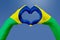 Hands flag of Brazil, shape a heart. Concept of country symbol, on blue sky.