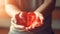 Hands gently holding a transparent red heart in a tender gesture, illuminated by soft sunlight, conveying love and care