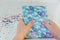 Hands of a girl holding notebook with llama unicorn and rainbow on white wooden background with confetti. Idea of Girly