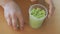 Hands of a girl picking up pieces of green kinetic sand in a plastic cup after playing