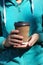 The hands of the girl in the turquoise sports case hold a brown glass with coffee