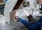 The hands of a glassblower woman holding a glass rod over the flame of a burner against the background of the workplace