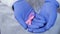 Hands in gloves carefully holds pink ribbon, symbol of breast cancer awareness