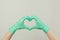 Hands in green doctor gloves making heart on gray background