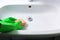 Hands in green rubber gloves clean sink in domestic bathroom yellow sponge and liquid foam detergent. Concept housework