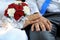 Hands of the groom and the bride with wedding rings and a wedding bouquet from roses and chrysanthemums