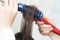 Hands of hairdresser dries brunette hair using blue hairbrush, red hairdryer in beauty salon