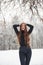 Hands on the head. Pretty girl with long hair and in black blouse is in the winter forest