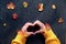 Hands of hipster woman with Autumn leaves in sleeves show heart sign. Natural Fall decorations, red and yellow Fall leaves. Flat