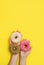 Hands hold delicious sweet donuts with frosting and filling on a yellow background. Favorite American pastry. vertical