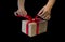 Hands hold gift box with red ribbon, copy space isolated on black. Sales concepts, discount price, christmas gifts