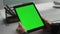 Hands hold green tablet at contemporary workplace closeup. Freelancer use chroma
