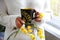 Hands holding a black and yellow mug with coffee and yellow meadow tulips on a window background. Home relaxation