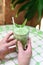 Hands holding blended brew matcha latte with straw on green table and wooden wall