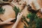 Hands holding fir branches and pine cones, thread, scissors on wooden table. Details for workshop of making christmas wreath.