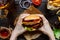 Hands holding fresh delicious burgers with french fries, sauce and beer on the wooden table top view