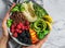 Hands holding fresh summer salad with quinoa, peach, micro greens, avocado, berries, coconut, melon on light marble background.