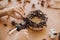 Hands holding glue gun and making rustic festive decoration from  pine cones, branches, and cotton on wooden table. Holiday