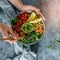 Hands holding healthy superbowl or Buddha bowl with salad, baked sweet potatoes, chickpeas, broccoli, hummus, avocado, sprouts on