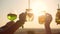 Hands holding high four glasses with cocktails against background of bright sun, closeup. Friends hold their glasses