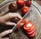 Hands holding a knife slicing a tomato