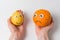 Hands holding an orange with sad face and cheerful lemon with smile. Food character with eyes and smile