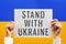 Hands holding poster with text Stand With Ukraine