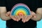Hands Holding A Rainbow. A beautiful, colorful, wooden rainbow in the hands of a young girl on a blue background. A symbol of peac
