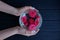 Hands holding a round glass vase with buds of red roses in the water