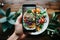 Hands holding smartphone capturing appetizing dishes with professional photography